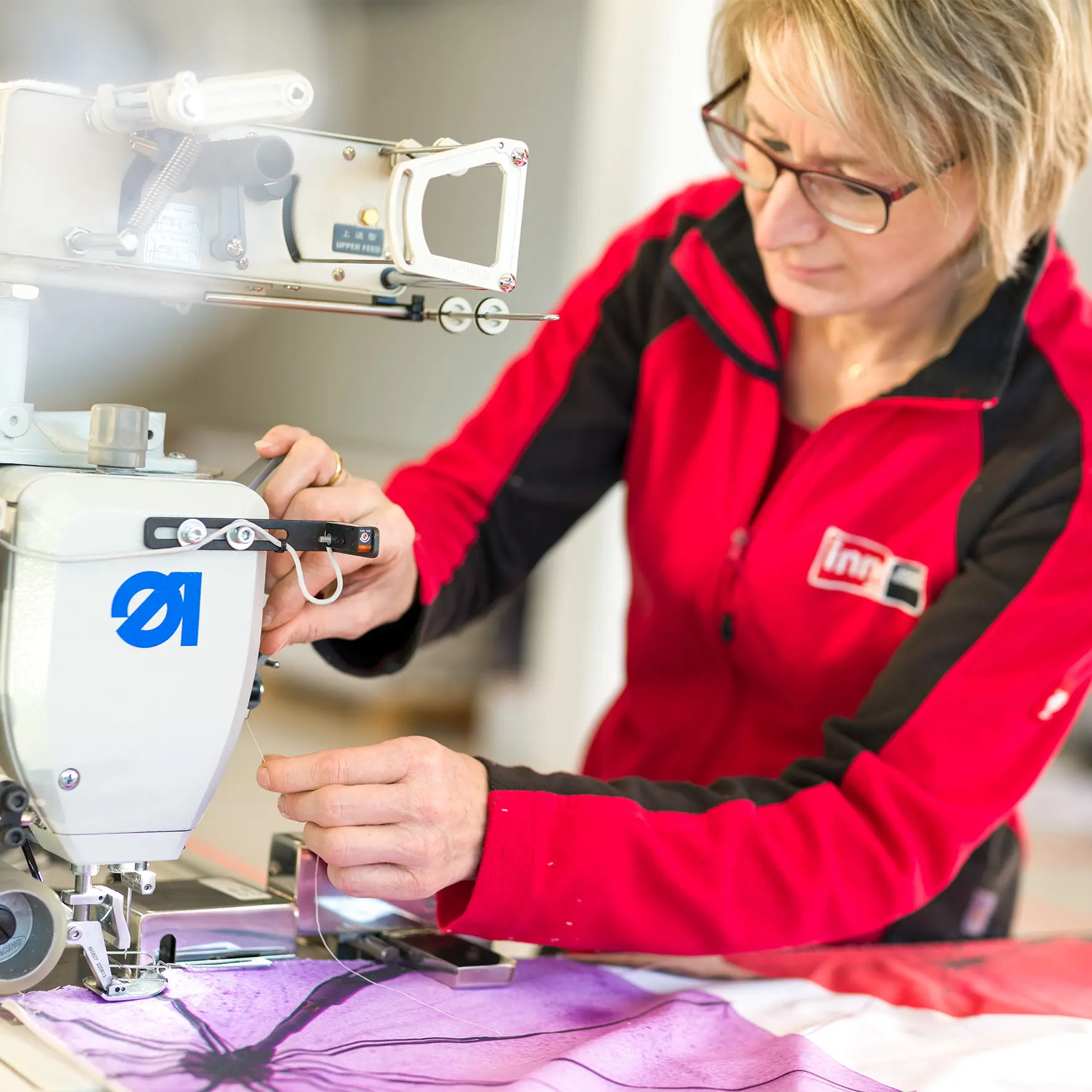 Mitarbeiterin beim Nähen eines Flachkeders an einen Textildruck