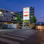 Beleuchteter Werbeturm auf Parkplatz – Logo und Schriftzug sichtbar