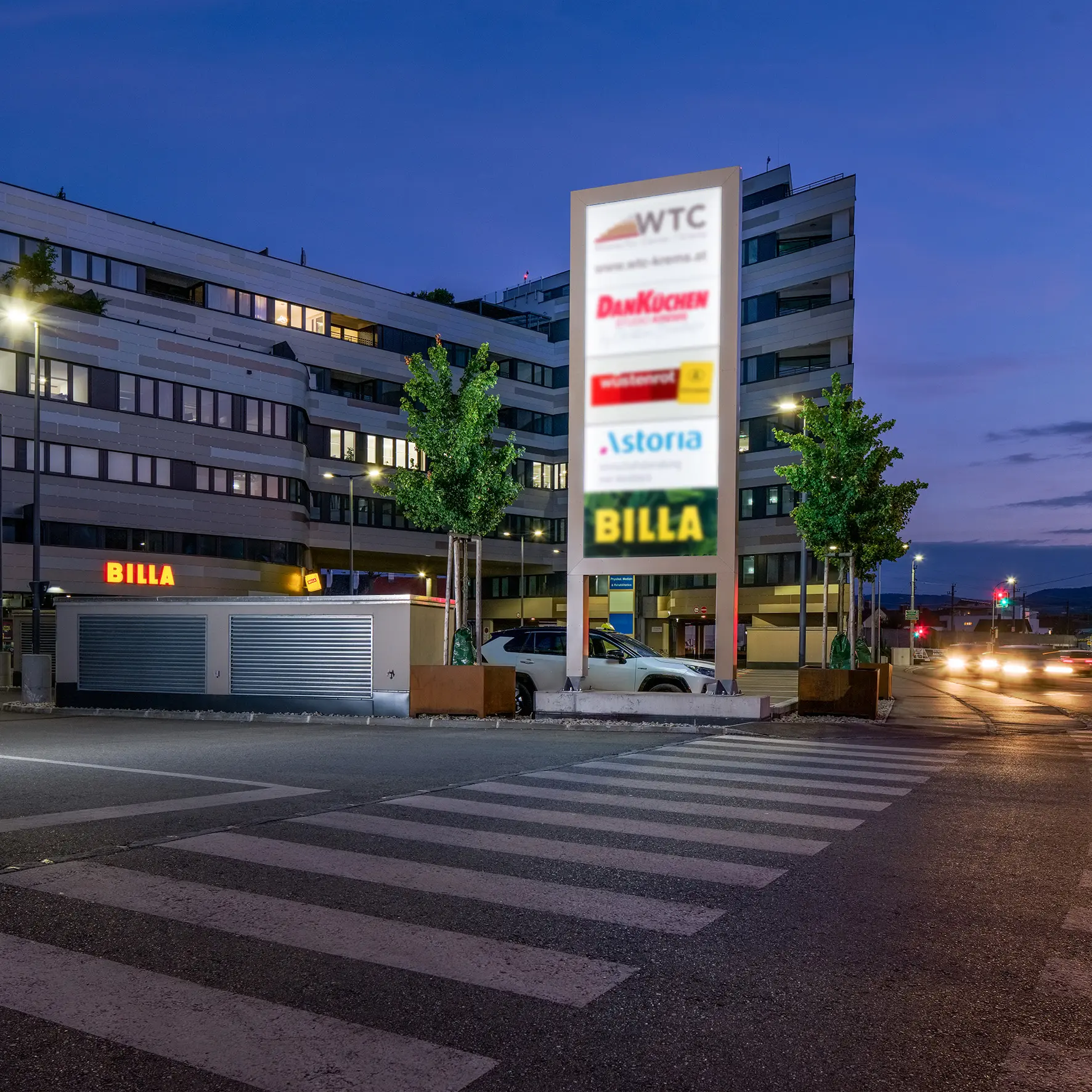 Beleuchteter Werbeturm auf Parkplatz – Logo und Schriftzug sichtbar